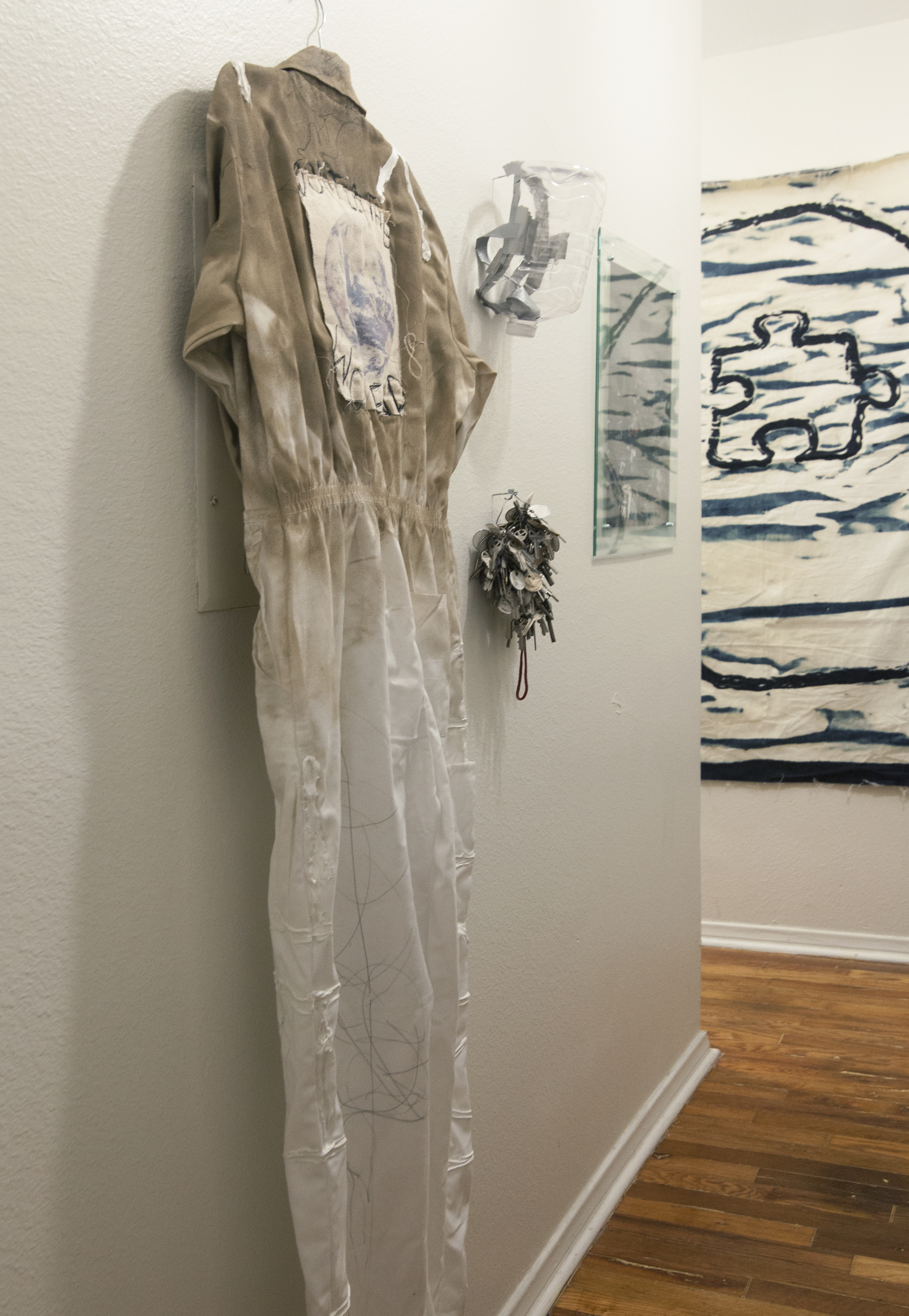 A white dirty jump suit, keys and mask hung on a white wall